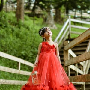 A young girl in a beautiful red dress walks on a wooden path surrounded by greenery.